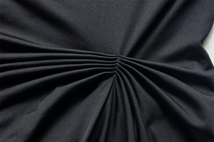 Close-up of radial pleated details and high-quality black knit fabric texture on the dress