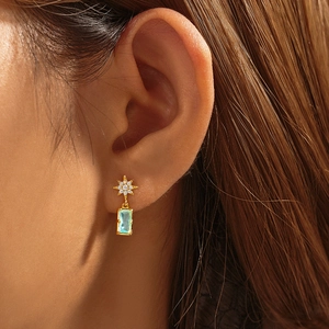 Detail of gold star earring with light blue emerald-cut gemstone on a model's ear