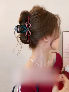 Détail d'une pince à cheveux à nœud rouge et rose portée sur des cheveux ondulés