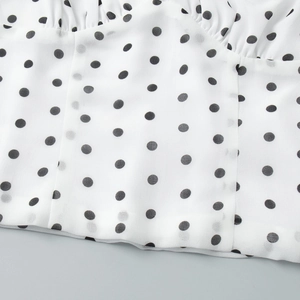 Detailed close-up of white polka dot fabric with refined pleated texture and neat stitching
