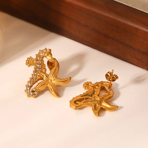 Vue macro de boucles d'oreilles hippocampe et étoile de mer dorées avec strass blancs
