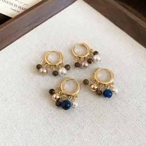 Detail of 18k gold plated earrings featuring tiger eye beads and pearls in a wooden tray