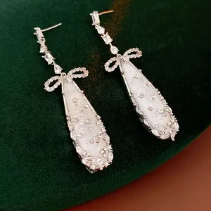 Silver bow and teardrop zircon earrings displayed on a dark luxury velvet background