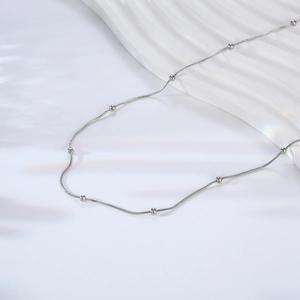 Elegant silver snake chain necklace with beads on minimalist white textured background