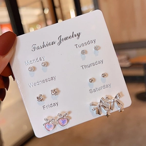 Close-up of 6 pairs of silver earrings on a weekly card including pearls and crystals