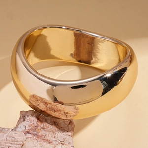 Close-up of a wide polished gold bracelet with irregular geometric design on a natural rock