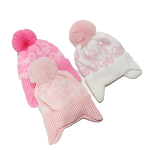 Detail of winter knitted beanies with plush pompoms and bow patterns in three colors