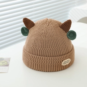 Close-up of thick knitted winter hat with cute brown horns and green round ear accents