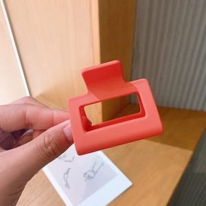 Detail shot of a square matte orange hair claw clip held by hand over a wooden desk