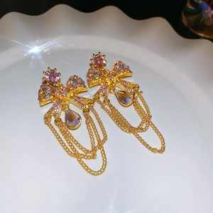Macro shot of gold bow tassel earrings with pink crystals on white ceramic tray