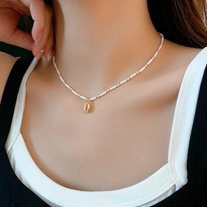 Close-up of bohemian beaded necklace with white seed beads and golden shell pendant