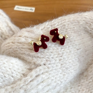Detail of burgundy flocked horse stud earring on a cream knitted sweater background
