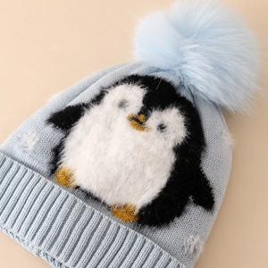 Light blue winter knit hat for boys featuring a plush penguin patch and large faux fur pom