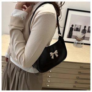 Side view of a black glossy baguette bag featuring a silver 3D bow and thin strap