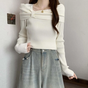 Detail view of the ribbed knit texture and bow-knot off-shoulder neckline on white sweater