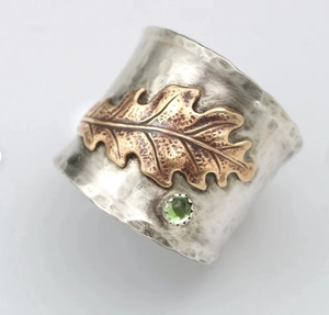 Detailed close-up of a wide hammered silver ring with golden oak leaf and green gemstone