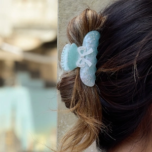 Detail of light blue bow hair claw clip with rhinestones worn on dark hair