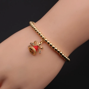 Détail d'un bracelet en perles dorées avec pendentif cloche en émail rouge et nœud en zircon