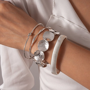 Detail view of silver geometric bangles stack with hammered and ribbed textures on wrist
