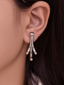 Détail des boucles d'oreilles argentées avec branches géométriques et zircons brillants
