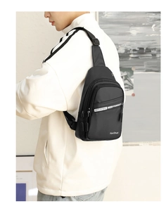 Side view of a trendy black nylon sling bag with multiple zippers worn by a male model
