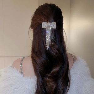 Détail d'une pince à cheveux nœud argentée scintillante avec glands sur cheveux longs
