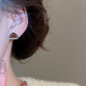 Detailed close-up of crown stud earrings featuring a warm brown pearl and micro-inlaid zircons