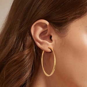 Minimalist large golden S925 sterling silver hoop earring worn by a female model