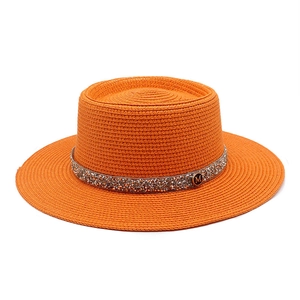 Detail of orange straw hat featuring sparkling rhinestone band and metal M logo