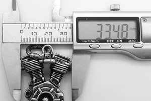 Macro shot measuring a 33mm stainless steel V-twin motorcycle engine pendant with calipers