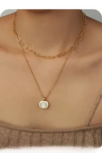 Detail of layered gold paperclip chain and bead necklace with white shell oval pendant
