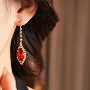 Close-up of elegant gold drop earring with red oval gemstone and sparkling rhinestones