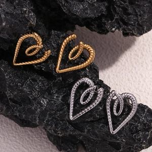 Detail of gold and silver twisted rope heart earrings on a dark textured stone background
