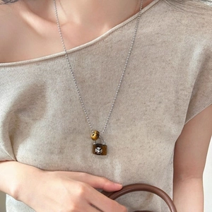 Detail of tiger eye heart pendant necklace with cross emblem on a model sweater