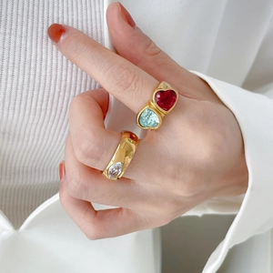 Close-up of gold titanium rings with heart-shaped red and blue stones on hand