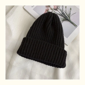 Close-up of black ribbed knit beanie featuring elastic texture on a minimalist background