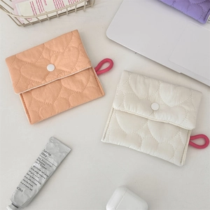 Detail of heart-quilted sanitary pouches in pink and cream with side loops on a desk