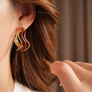 Detail view of irregular wavy gold earrings with dark red enamel on a model ear