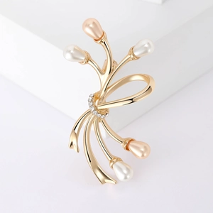 Broche nœud dorée avec perles champagne et strass scintillants sur support géométrique