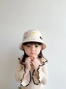 Detail of a beige kid fisherman hat with colorful bows and a decorative woven patch