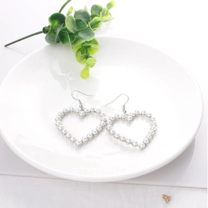 Detail view of heart-shaped pearl drop earrings on white plate with greenery accents