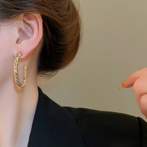 Close-up of model wearing gold-toned twisted C-shape hoop earrings with spiral texture