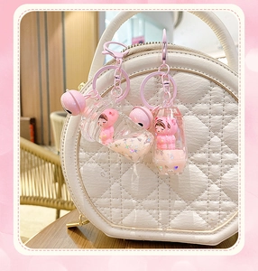 Detailed view of pink liquid quicksand keychain charm on a white quilted handbag