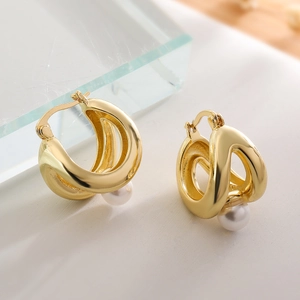 Aros elegantes bañados en oro de 18K con perlas blancas sobre una superficie blanca