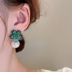 Close-up of pearl drop earrings with green crystal flower studs worn by a model