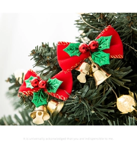 Close-up of red velvet Christmas bow with gold bells hanging on a green festive tree