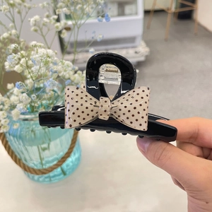 Black claw clip with beige polka dot bow accent shown against a floral background