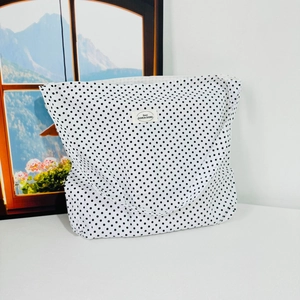 Detail view of a white canvas tote bag with black polka dots and a small branded label