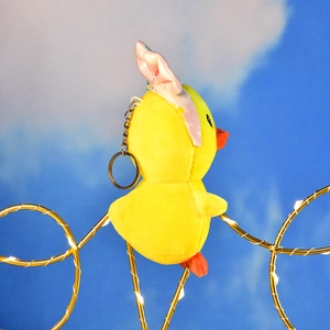 Side view detail of a cute yellow plush duck keychain wearing a pink bow headband