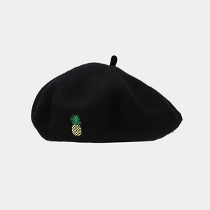 Détail d'un béret en laine noire avec une broderie délicate en forme d'ananas jaune